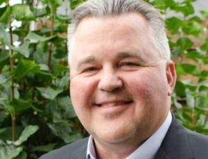man smiling in front of greenery