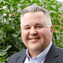 man smiling in front of greenery
